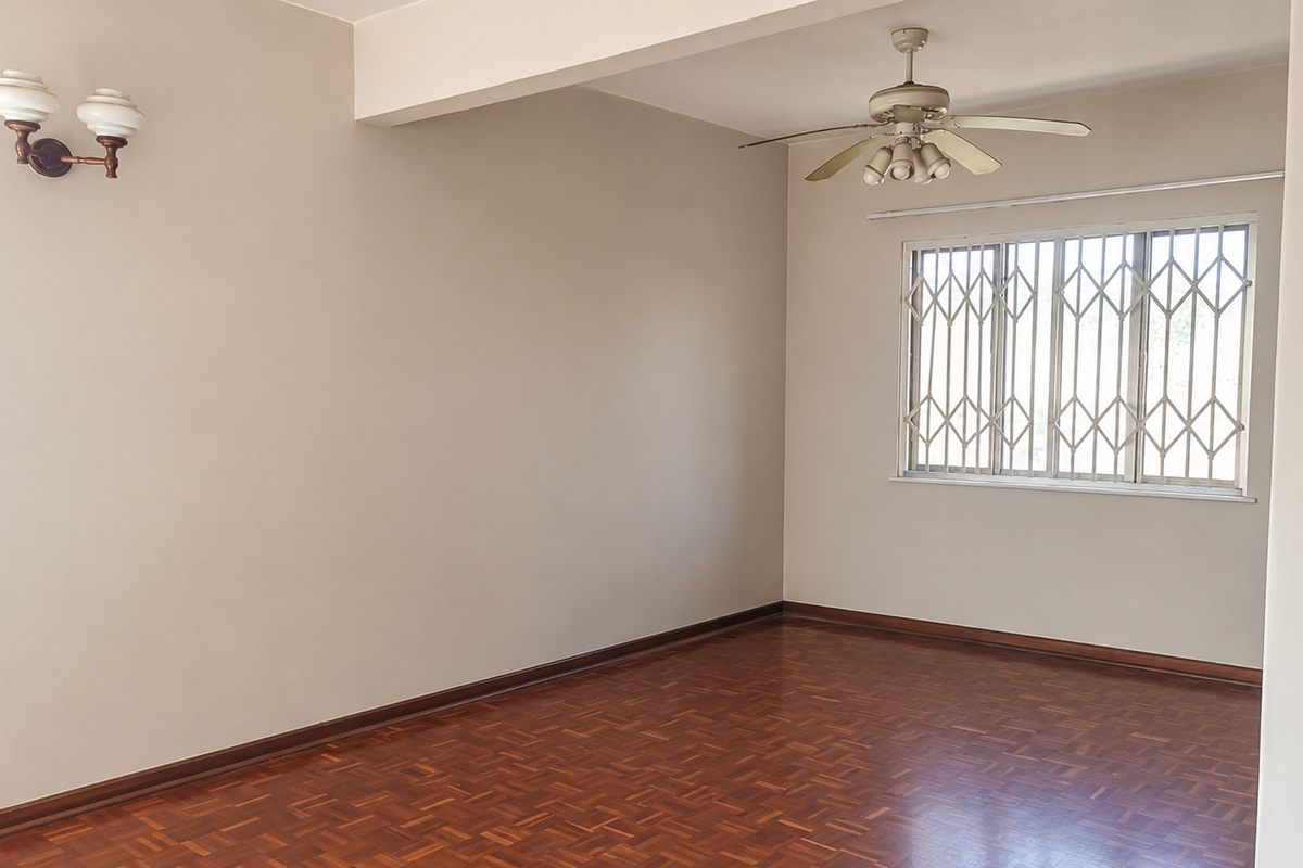 A spacious, empty living room featuring polished parquet flooring, a ceiling fan, and a window fitted with a security gate.