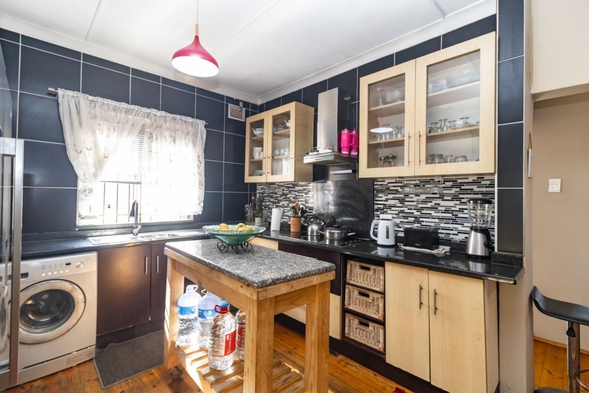 A functional kitchen featuring dark tiled walls, light wood cabinetry, granite countertops, and a central island, providing a practical workspace with integrated appliances.