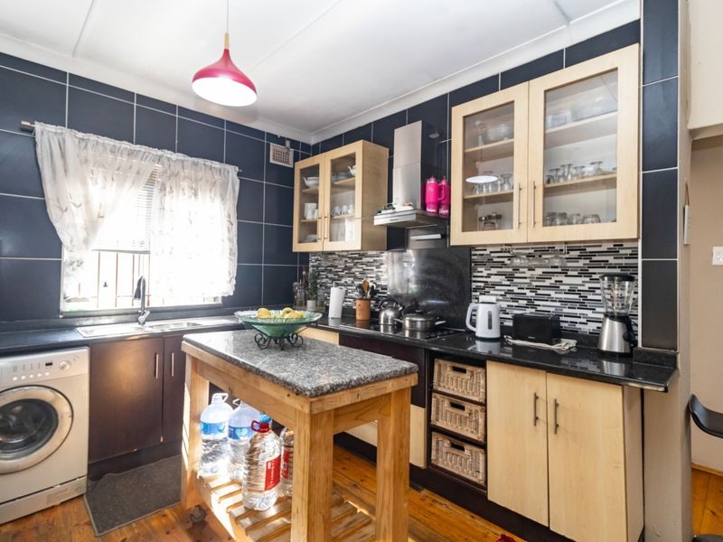 A functional kitchen featuring dark tiled walls, light wood cabinetry, granite countertops, and a central island, providing a practical workspace with integrated appliances.