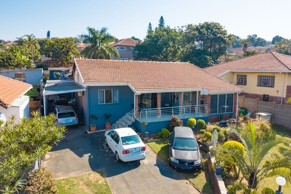 Aerial view of a residential property featuring a tiled roof, a covered front patio with metal railings, and a paved driveway with carport.