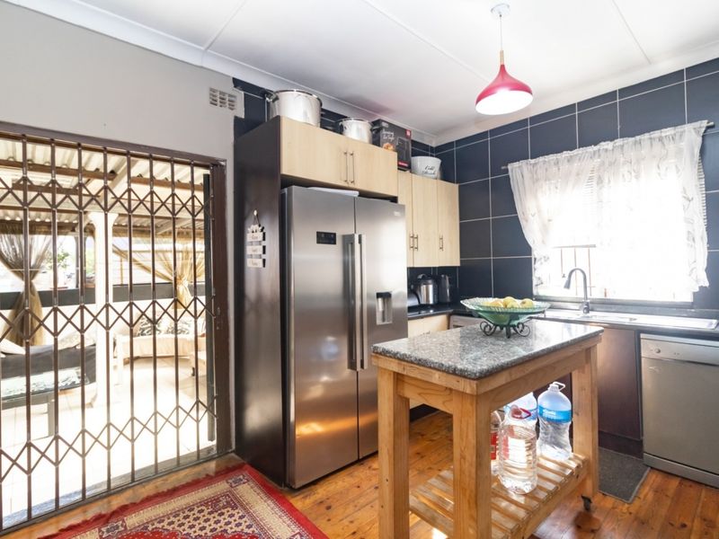 A functional kitchen featuring built-in cabinetry, granite countertops, and a tiled splashback, with direct access to an outdoor patio area through a security gate.