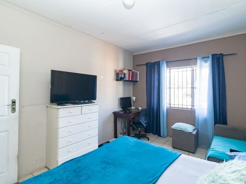 A functional bedroom featuring tiled flooring, security bars on the window, and an integrated air conditioning unit.