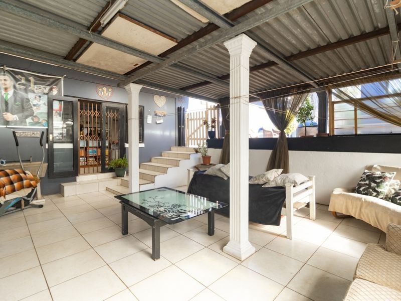 A covered outdoor patio area featuring tiled flooring, decorative columns, and a corrugated metal roof, providing a functional space for outdoor living.