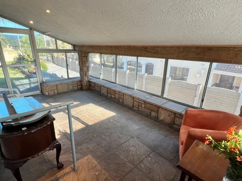 A sun-drenched enclosed patio featuring stone-clad walls, large windows providing ample natural light, and durable tiled flooring, ideal for a relaxed seating area.