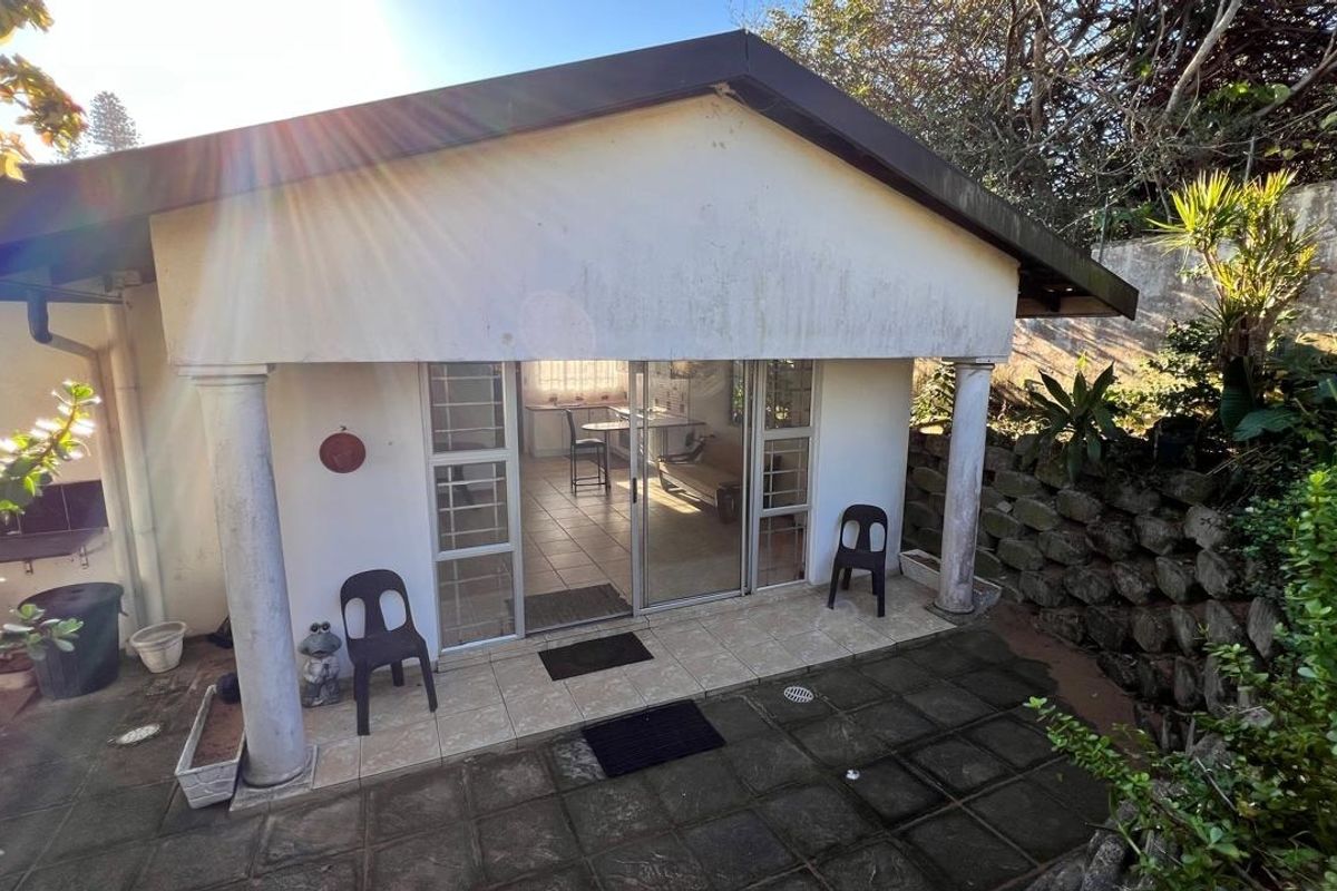 Rear exterior view of the property featuring a tiled patio area, sliding glass doors, and a stone retaining wall.