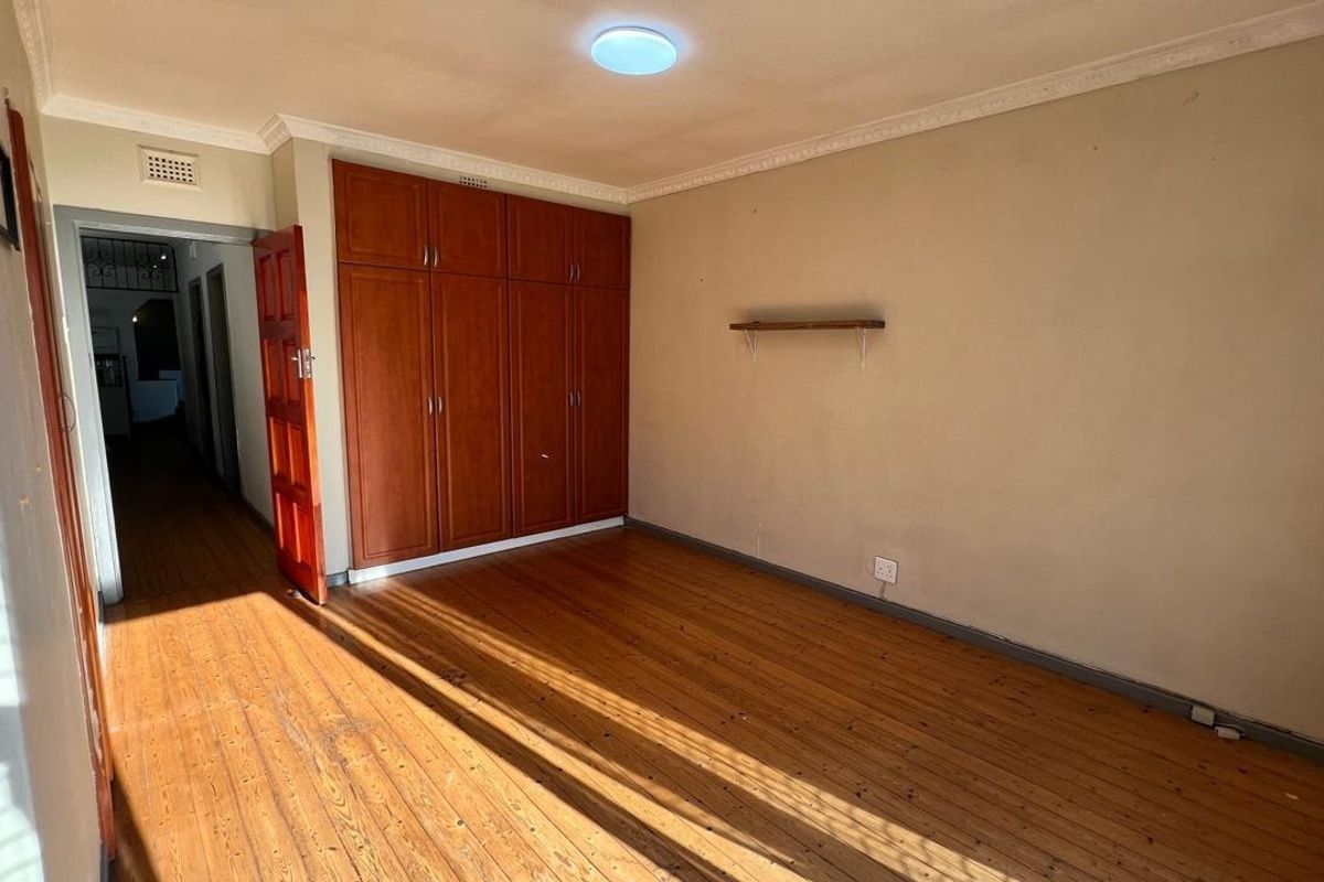 A vacant bedroom featuring original wooden flooring, built-in wooden cupboards, and classic ceiling cornicing, offering a blank canvas for renovation.