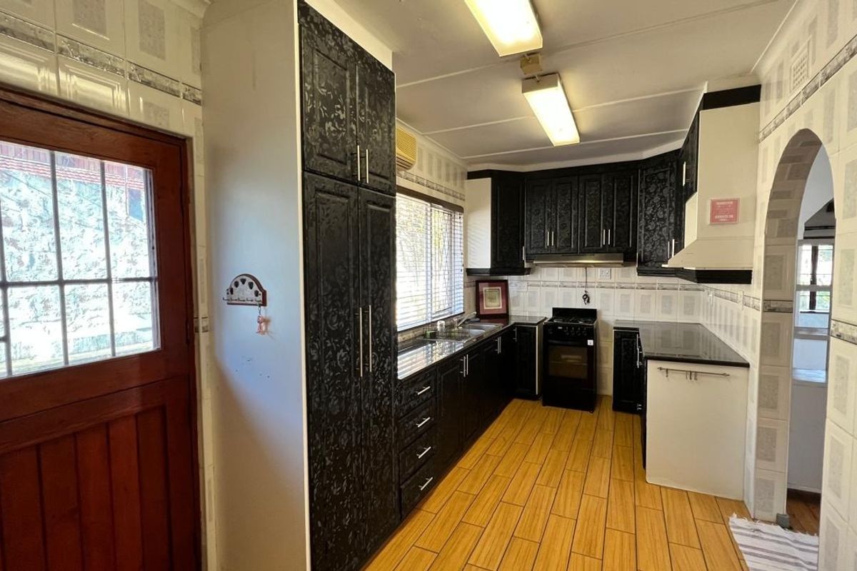 A functional kitchen featuring dark patterned cabinetry, a freestanding stove, extractor fan, and tiled finishes throughout, leading into an adjacent living space via an archway.