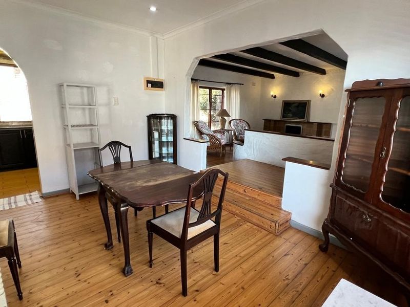 Open-plan living and dining area featuring timber flooring, exposed ceiling beams, and a split-level layout connecting to the kitchen.