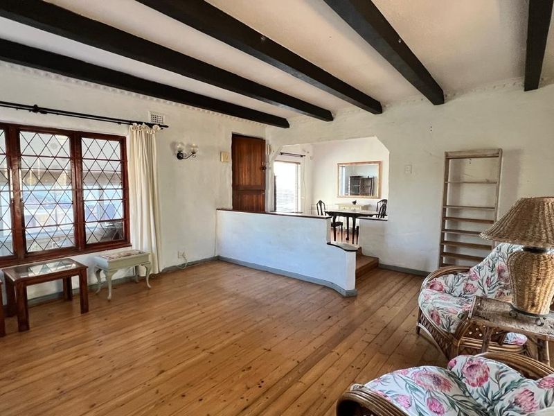 Open-plan living area featuring exposed timber ceiling beams, original timber flooring, and characterful leaded glass windows with a split-level layout.