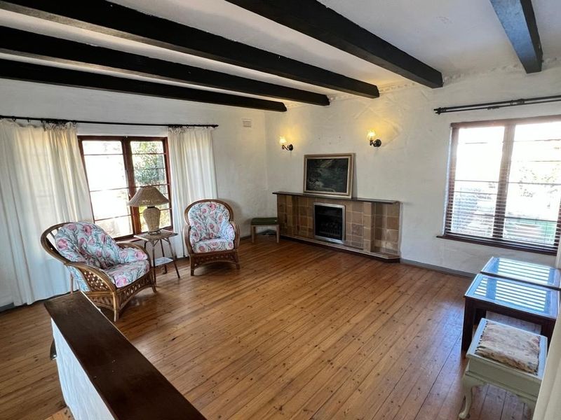 Spacious living room featuring exposed timber ceiling beams, polished timber flooring, and a classic tiled fireplace surround, offering a warm and character-filled atmosphere.