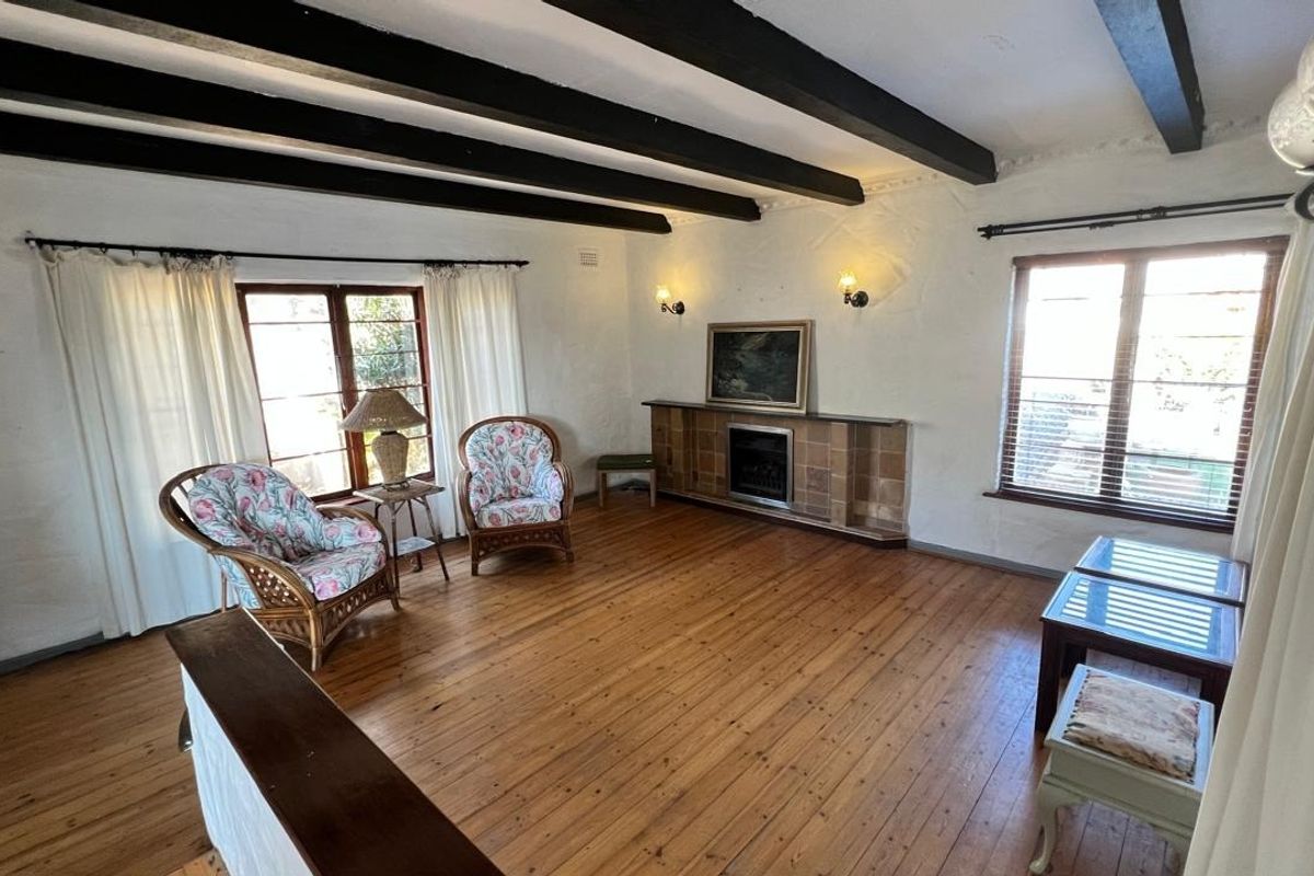 Spacious living room featuring exposed timber ceiling beams, polished timber flooring, and a classic tiled fireplace surround, offering a warm and character-filled atmosphere.