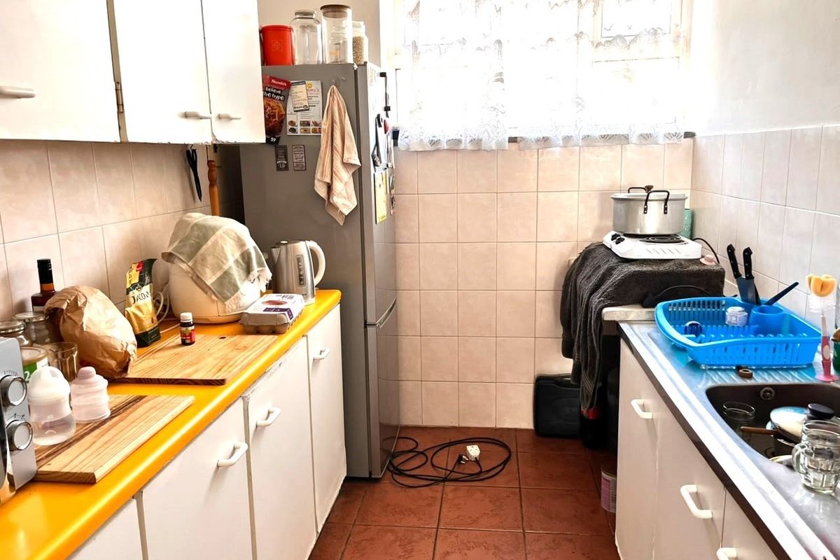 A compact galley-style kitchen featuring white cabinetry, a yellow laminate countertop, tiled backsplash, and tiled flooring, offering a functional layout for renovation.