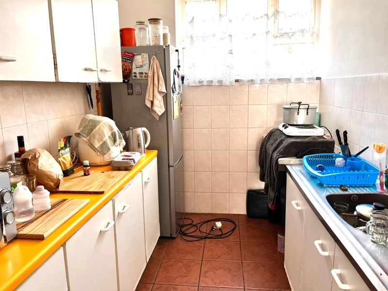 A compact galley-style kitchen featuring white cabinetry, a yellow laminate countertop, tiled backsplash, and tiled flooring, offering a functional layout for renovation.