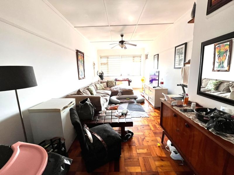 A living room featuring classic parquet flooring, a ceiling fan, and natural light provided by horizontal window blinds.