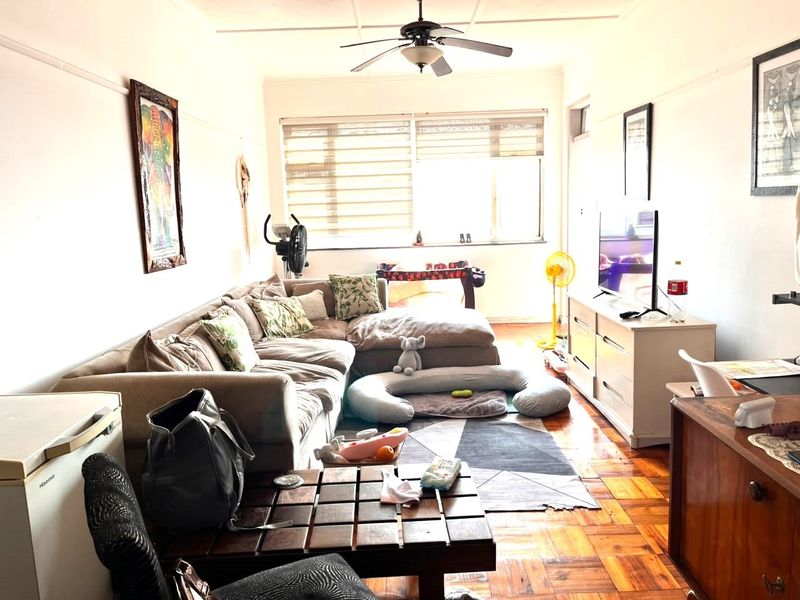 A living room featuring classic parquet flooring, a ceiling fan, and a large window that provides natural light to the space.