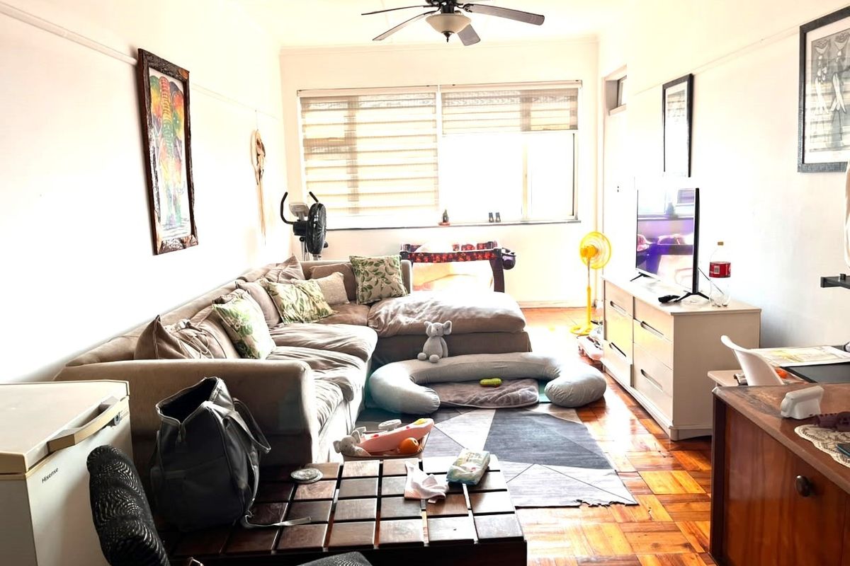 A living room featuring classic parquet flooring, a ceiling fan, and a large window that provides natural light to the space.