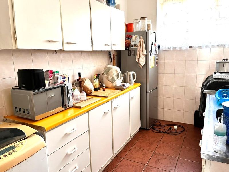 A functional kitchen featuring tiled flooring, a tiled backsplash, and built-in cabinetry with a laminate countertop, offering potential for modernization.