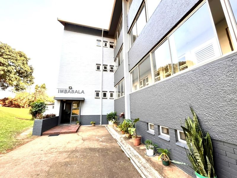 Exterior view of the Imbabala apartment building entrance, featuring a paved driveway and multi-story brick facade with sliding windows.