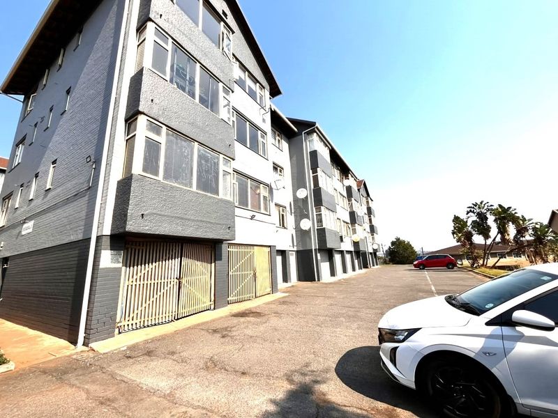 Exterior view of a multi-story apartment building featuring a paved driveway, security gates, and visible facade maintenance requirements.
