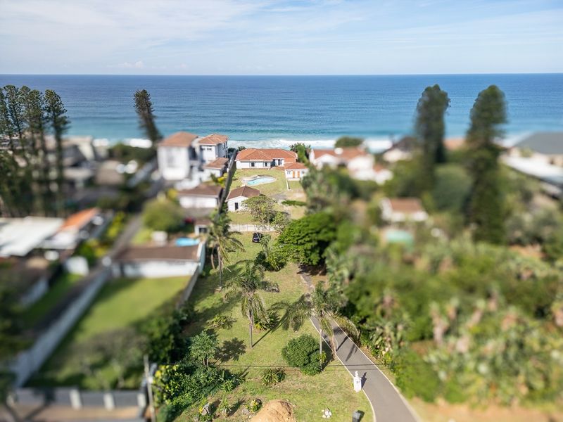 Aerial view of a coastal residential property featuring a large garden, swimming pool, and direct proximity to the ocean.