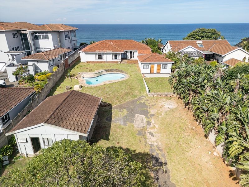 Aerial view of a coastal property featuring a swimming pool, large garden, multiple outbuildings, and direct ocean views.