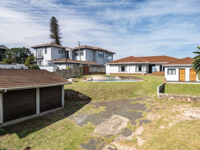 Rear view of the property featuring a swimming pool, detached garage, and a large garden area with a paved driveway.