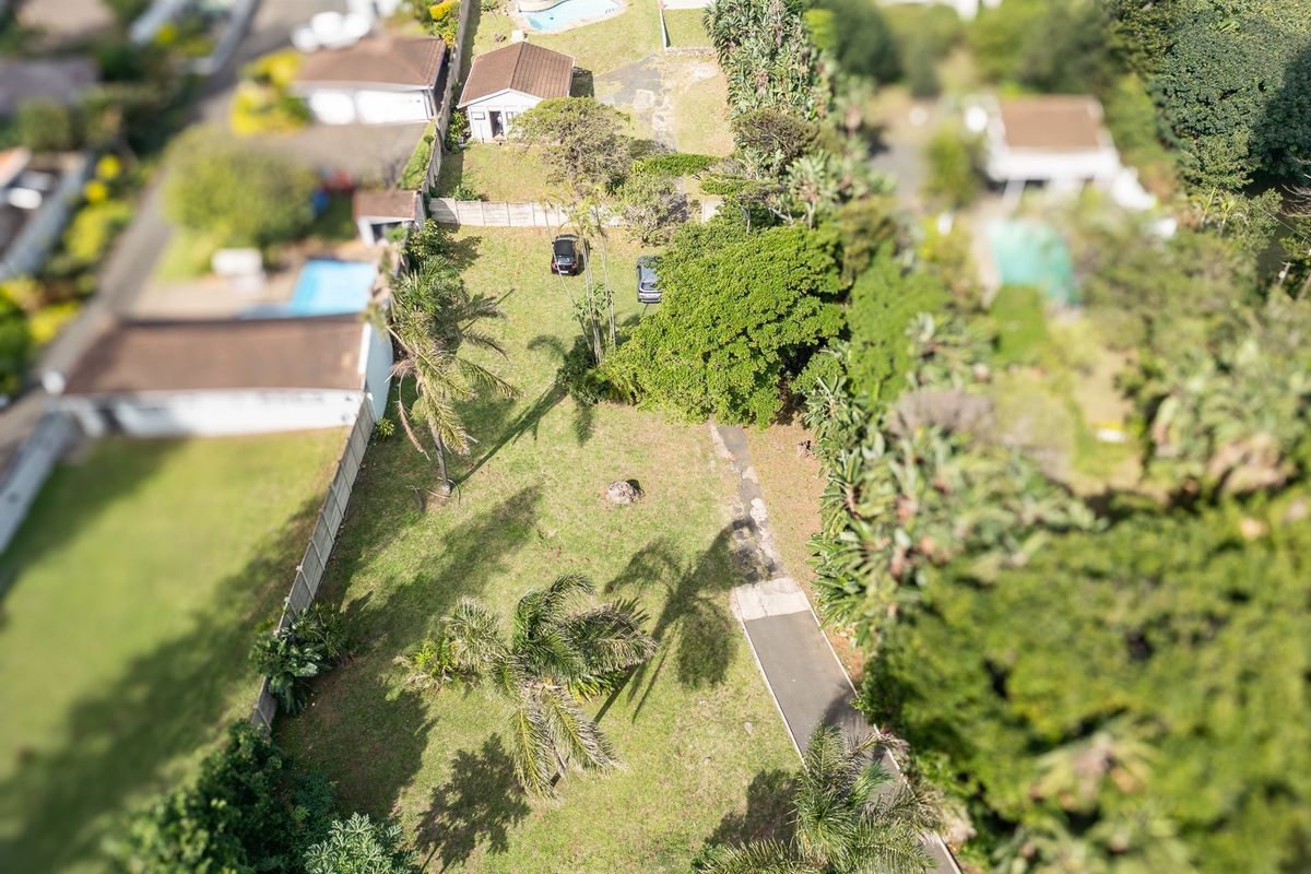 An aerial view of a residential property featuring a large garden, paved driveway, and established boundary fencing within a suburban neighborhood.