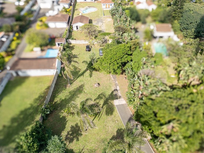 An aerial view of a residential property featuring a large garden, paved driveway, and established boundary fencing within a suburban neighborhood.