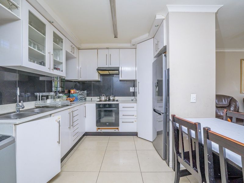 A functional kitchen featuring white cabinetry, stone countertops, a built-in oven with hob, and tiled flooring, offering a practical layout for daily meal preparation.