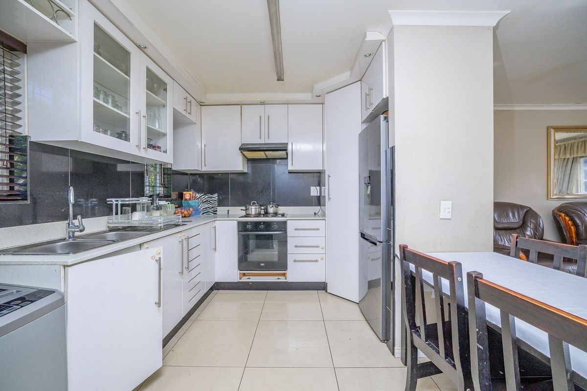 A functional kitchen featuring white cabinetry, stone countertops, a built-in oven with hob, and tiled flooring, offering a practical layout for daily meal preparation.