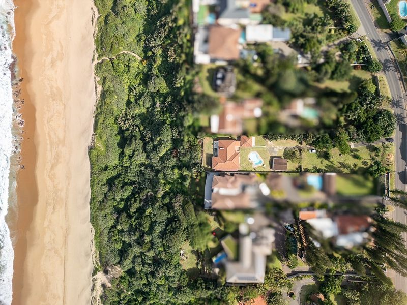 Aerial view of a coastal residential property featuring a swimming pool, tiled roof, and direct proximity to the beach and natural vegetation.