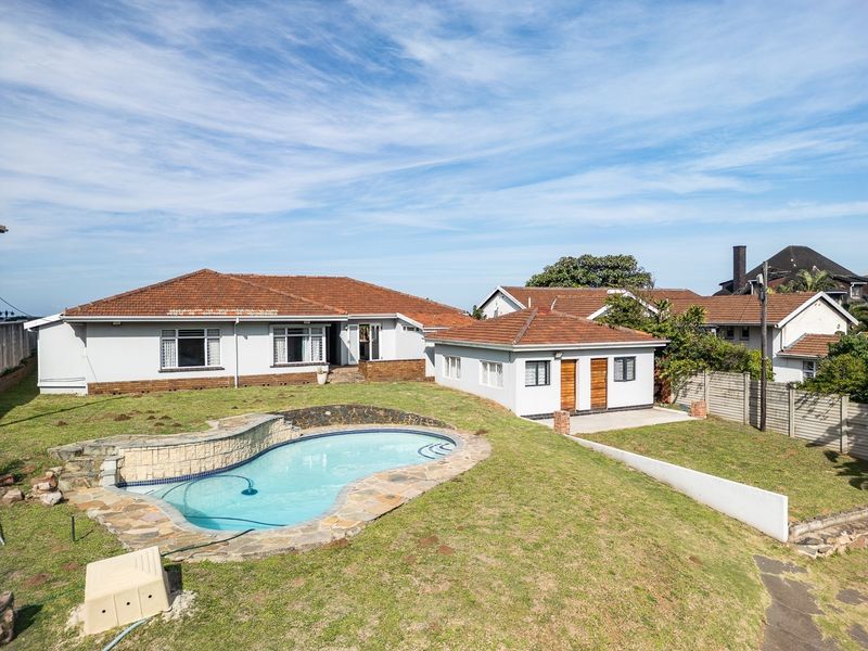 Rear view of the property featuring a swimming pool with stone surround, a spacious lawn, and a detached outbuilding under a tiled roof.