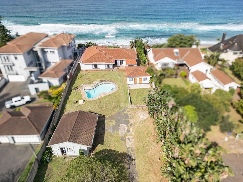 Aerial view of a coastal property featuring a swimming pool, multiple structures, and direct proximity to the ocean.