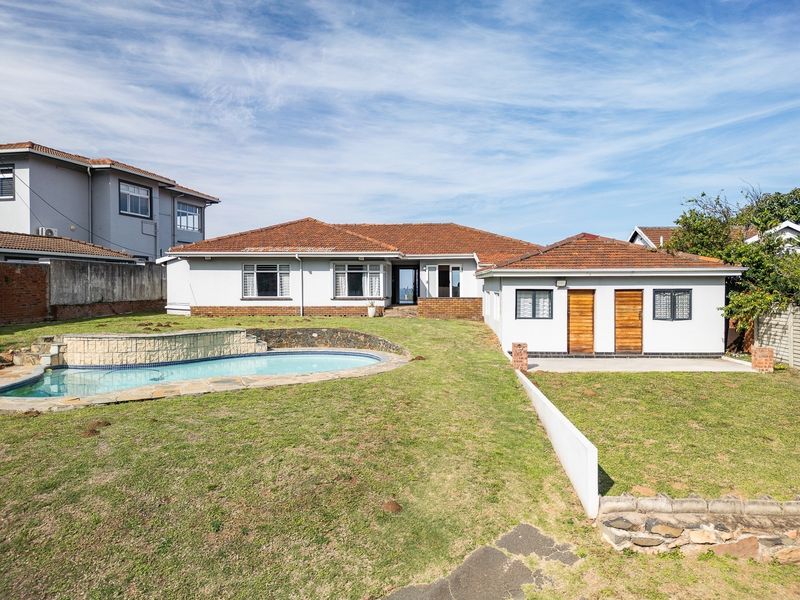Rear view of the property featuring a swimming pool, landscaped lawn, and a detached outbuilding with wooden doors.