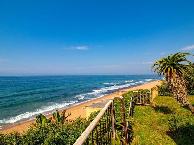 A scenic coastal view overlooking the beach, featuring a weathered metal railing and natural garden surroundings.