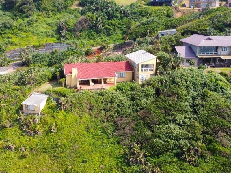 Aerial view of a residential property featuring a red roof, covered patio, and surrounding lush coastal vegetation.