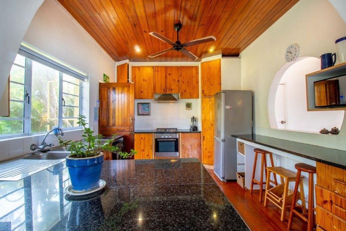 A functional kitchen featuring warm wooden cabinetry, granite countertops, a breakfast bar, and a distinctive wooden ceiling with an integrated fan.