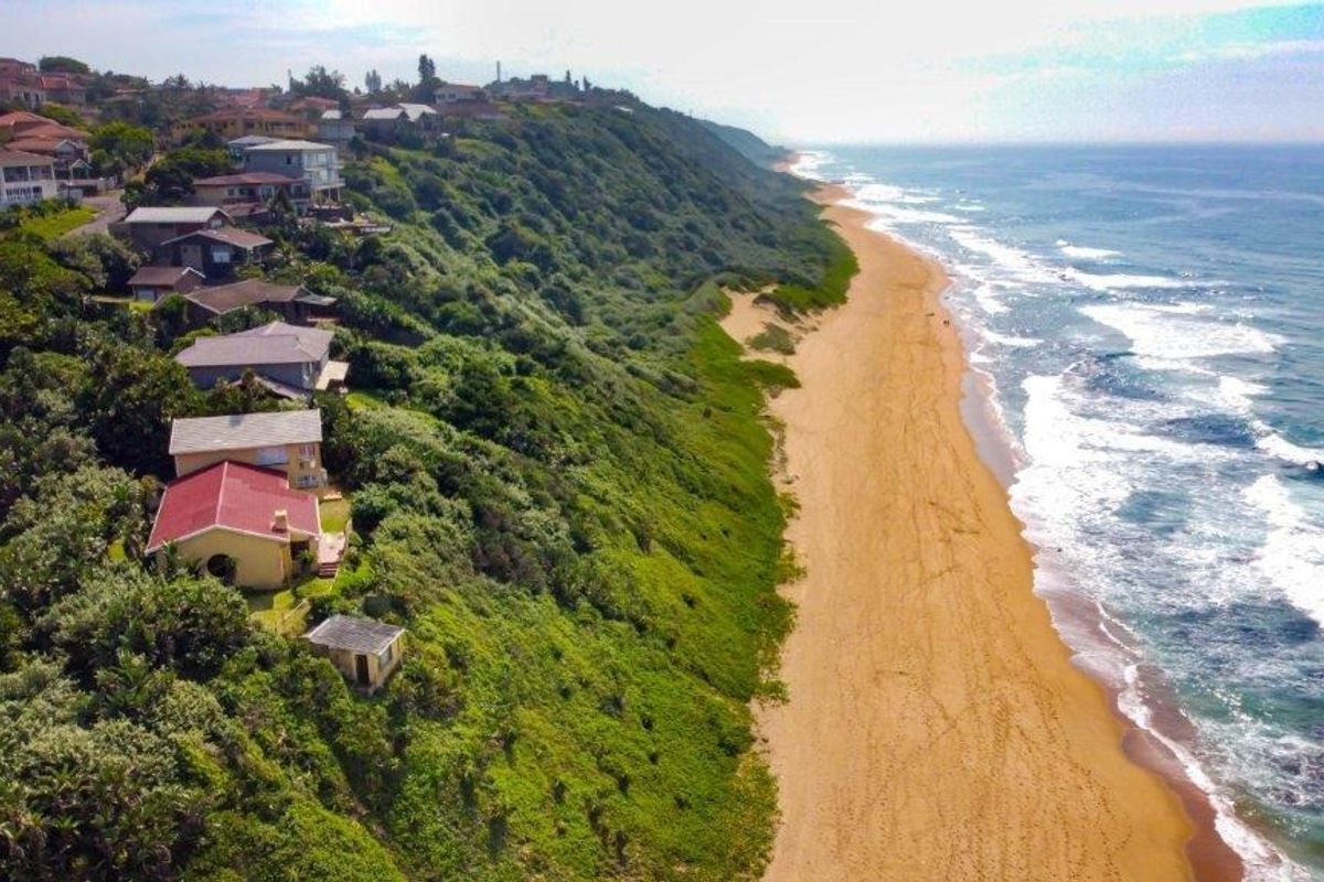 An aerial view of a coastal residential area situated on a cliff overlooking the sandy beach and ocean.