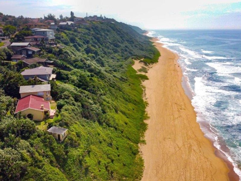 An aerial view of a coastal residential area situated on a cliff overlooking the sandy beach and ocean.