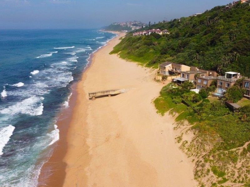 An aerial view of a coastal residential complex situated directly along the sandy beach and ocean shoreline.