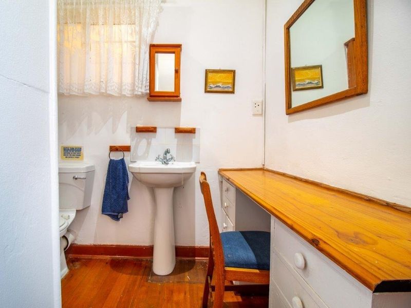 A functional bathroom featuring a pedestal sink, tiled splashback, and a built-in timber vanity desk with storage drawers.