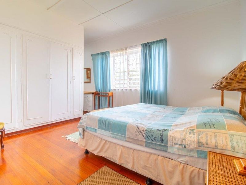 A bedroom featuring polished wooden flooring, built-in cupboards, and a window fitted with security bars.