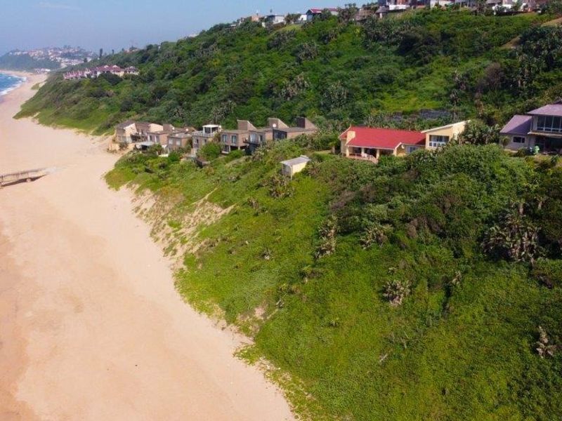 An aerial view of a coastal residential property situated on a hillside overlooking the beach and ocean.