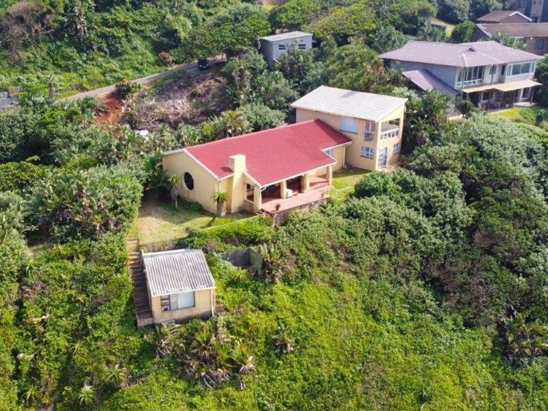Aerial view of a residential property featuring a main house with a red pitched roof, a covered patio, and a separate outbuilding set in greenery.