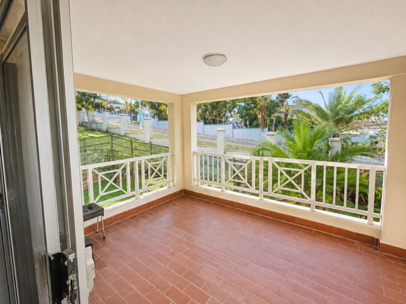 A covered balcony featuring terracotta-style tiled flooring and a white metal balustrade, offering an open view of the surrounding garden and neighborhood.