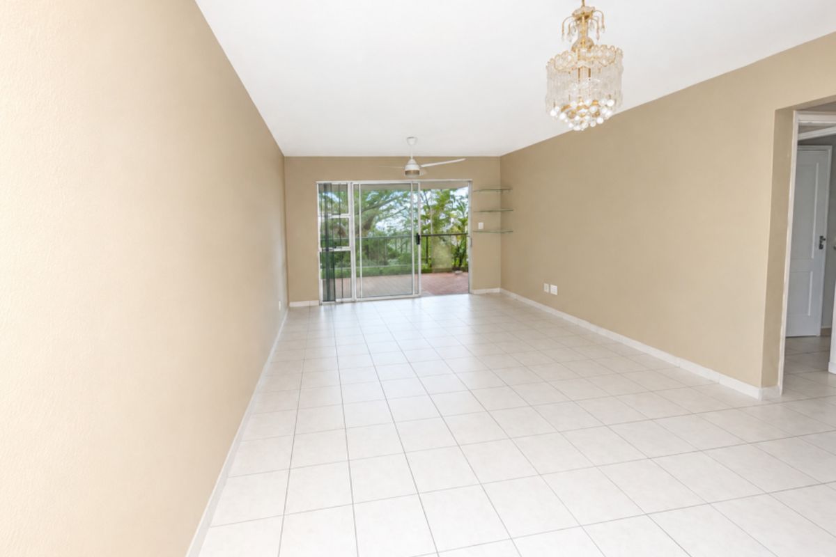 A spacious, empty living room featuring neutral tiled flooring, a ceiling fan, a decorative chandelier, and sliding glass doors leading to an outdoor area.