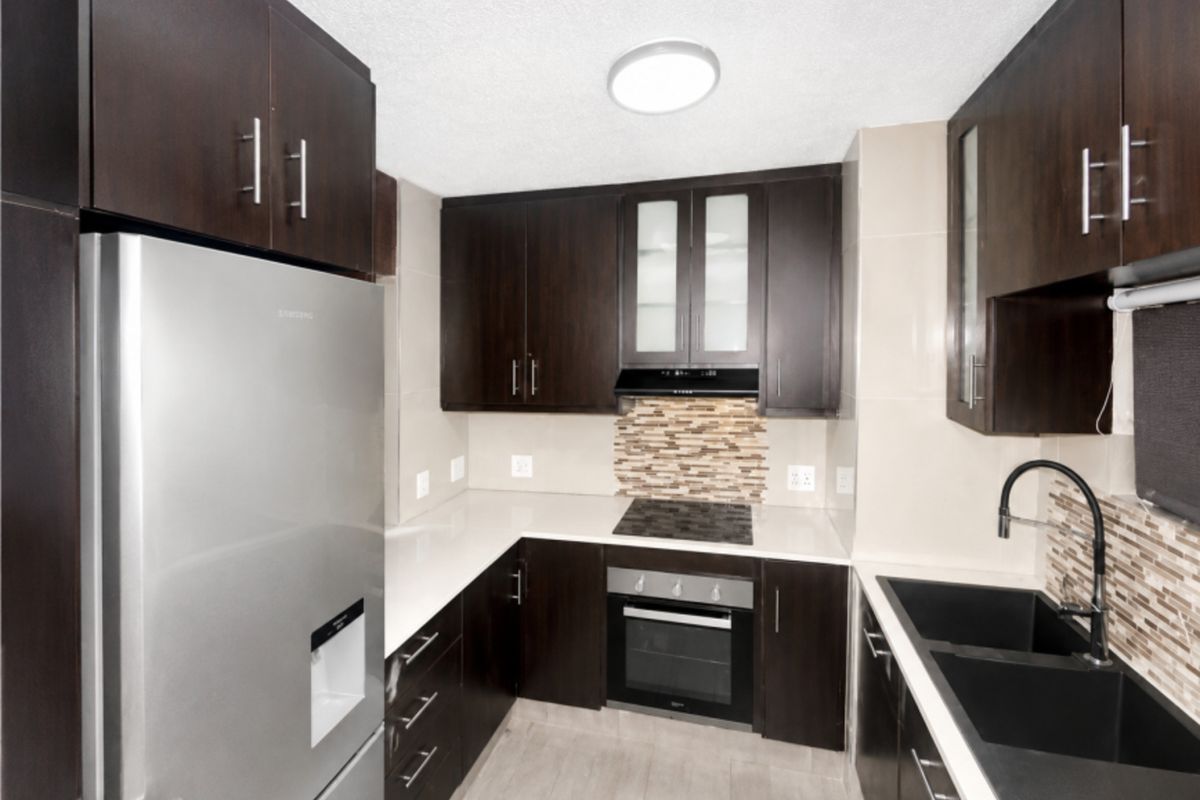 Modern kitchen featuring dark wood cabinetry, stone countertops, integrated oven and hob, and a contemporary double basin sink with tiled backsplash.
