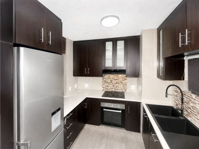 Modern kitchen featuring dark wood cabinetry, stone countertops, integrated oven and hob, and a contemporary double basin sink with tiled backsplash.