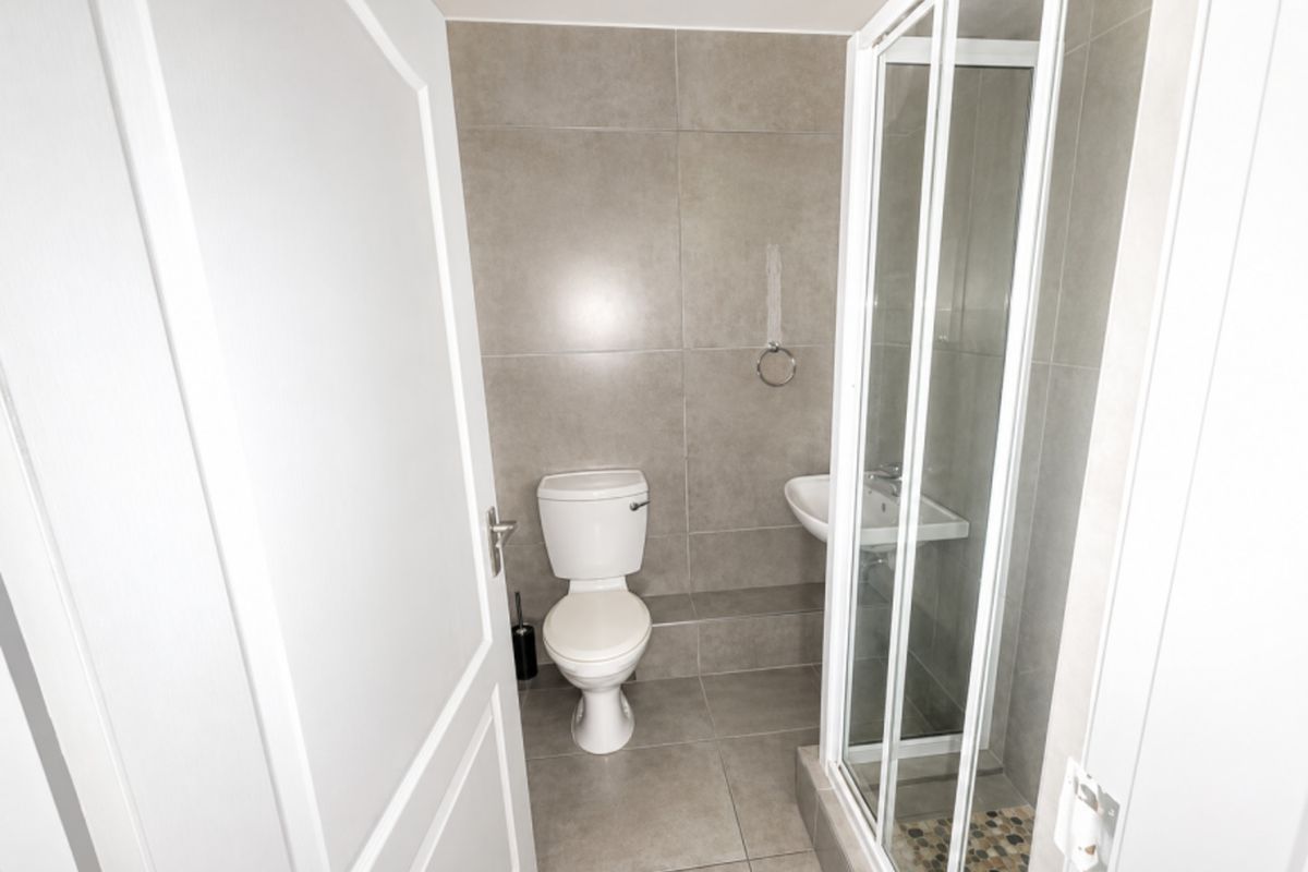 A compact, modern bathroom featuring neutral grey floor-to-ceiling tiling, a white toilet, a wall-mounted basin, and a glass-enclosed shower.