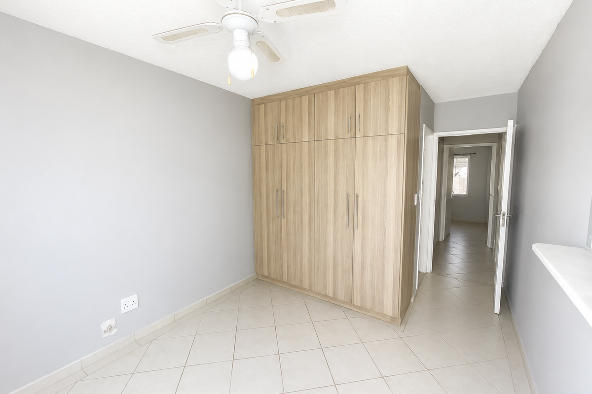 A bright, empty bedroom featuring light-toned built-in wardrobes, neutral tiled flooring, and a ceiling fan, offering a clean and versatile living space.
